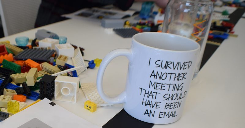 A mug reading “I survived another meeting that should have been an email” on a table covered in bricks